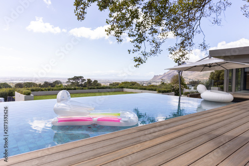 Translucent lounger is floating in infinity pool by wooden deck, with pink yellow strips
