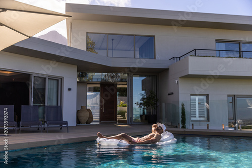 African American man lounging on clear float in briefs, wearing cap, sunglasses by pool, copy space