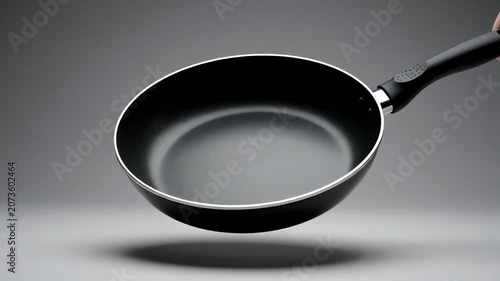 Black non-stick frying pan held by hand on grey background. 4K Video