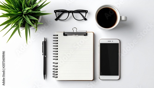 A cluttered desk with office supplies and a plant on a white surface viewed from above