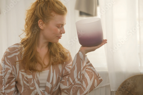 Young ginger woman holding a crystal singing bowl during a mindful sound healing session, immersed in meditation, vibration and inner harmony