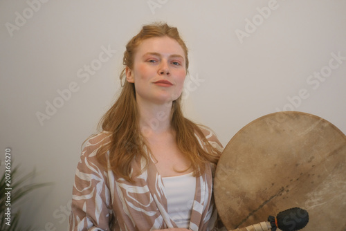 Young woman holding a traditional frame drum during a sound healing session. Calm expression, mindful presence and holistic wellness create an atmosphere of spirituality, meditation and inner harmony