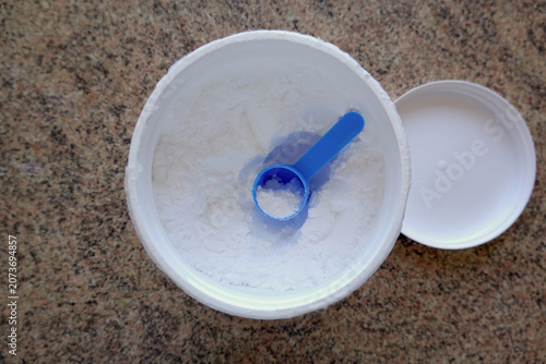 Top view of an open container with white creatine powder with a blue measuring scoop