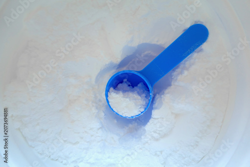 Top view of white creatine powder with a blue measuring scoop resting in the container