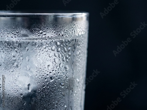 Close up of a cold glass filled with water and ice cubes covered in condensation droplets