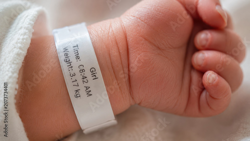 Close-up of a newborn tiny wrist wearing a hospital identification band with birth date and weight printed on it. Hospital birth concept