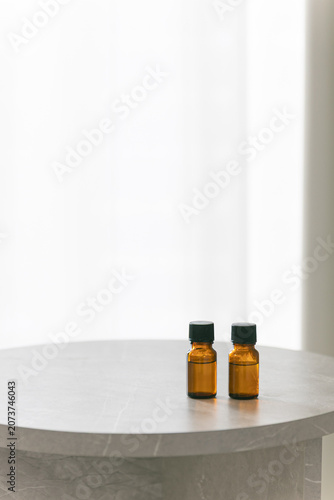 Two amber glass dropper bottles on a minimalist marble table, soft bright background with copy space for cosmetic or essential oil branding.