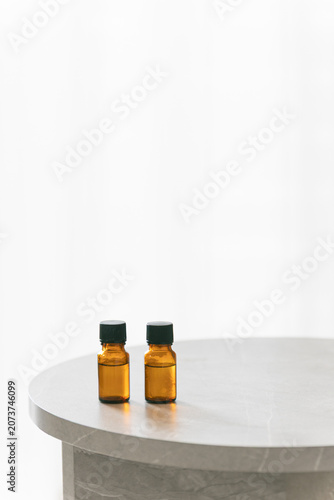 Two amber glass dropper bottles on a minimalist marble table, soft bright background with copy space for cosmetic or essential oil branding.