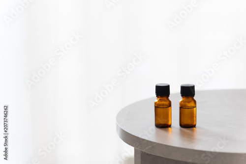 Two amber glass dropper bottles on a minimalist marble table, soft bright background with copy space for cosmetic or essential oil branding.