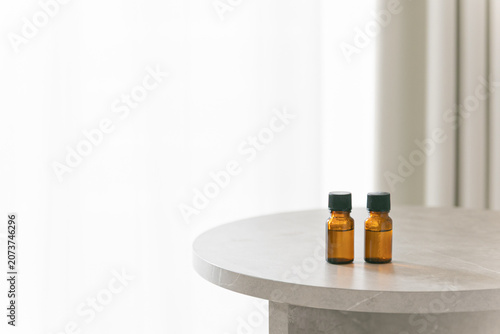 Two amber glass dropper bottles on a minimalist marble table, soft bright background with copy space for cosmetic or essential oil branding.