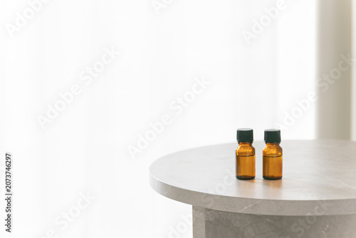 Two amber glass dropper bottles on a minimalist marble table, soft bright background with copy space for cosmetic or essential oil branding.