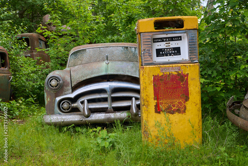 Yellow old fashioned gasoline pump with a classic antique automobile in an artsy still-life photograph