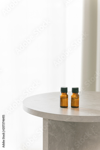 Two amber glass dropper bottles on a minimalist marble table, soft bright background with copy space for cosmetic or essential oil branding.