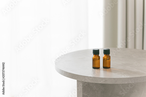 Two amber glass dropper bottles on a minimalist marble table, soft bright background with copy space for cosmetic or essential oil branding.