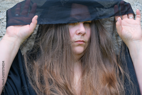 Portrait of a woman beneath a dark translucent veil. Concealed eyes and guarded expression create a concept of secrecy mystery identity emotion and introspection