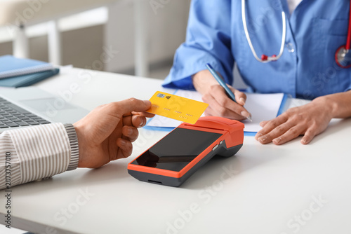 Male hand with credit card and doctor paying via terminal in clinic, closeup