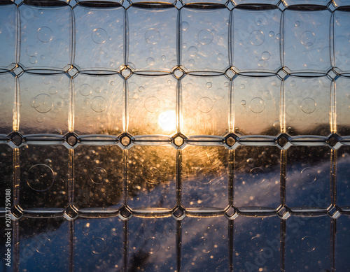 A serene sunset view through a hexagonal window with water droplets creating a prism effect on the glass.