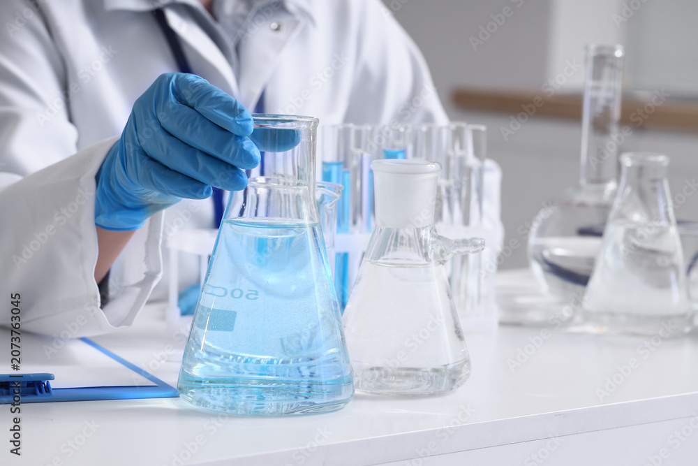 Fototapeta premium Female scientist with flasks of water samples at table in laboratory, closeup