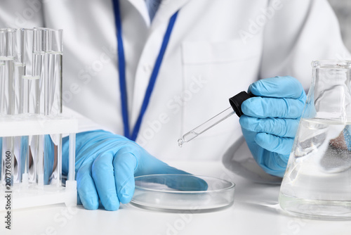 Female scientist dropping water sample onto Petri dish at table in laboratory...