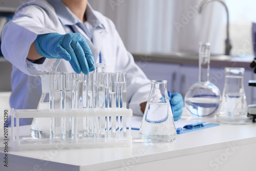 Female scientist with test tubes of water samples at table in laboratory