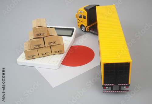 Cargo truck and heap of carton boxes on calculator with Japanese flag on grey background. Transportation cost in Japan concept.