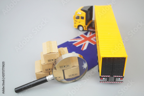 Cargo truck and heap of carton boxes under magnifying glass with Australian flag on grey background. Transportation in Australia concept.