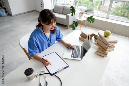 Female medical intern studying with laptop at table in clinic