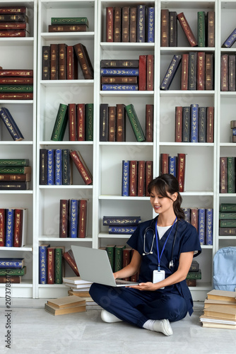 Female medical intern studying with laptop in library