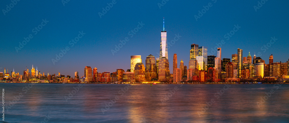 Obraz premium New York City panorama skyline. New York Freedom Tower glowing near NYC panorama. New York riverfront panorama at dusk. New York panoramic scene.