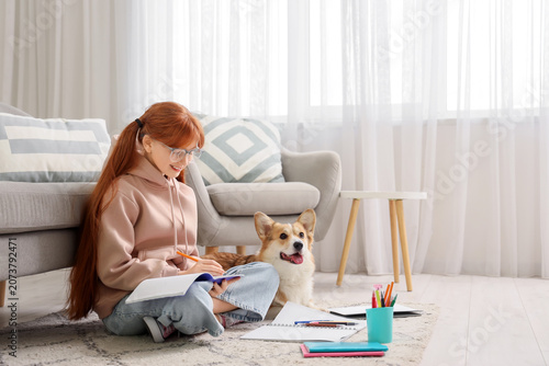 Teenage redhead girl with cute Corgi dog doing lessons at home