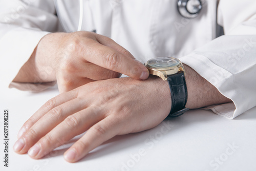 Close up of a male doctor checking his wristwatch. Healthcare and medical concept.