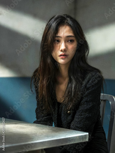 Worried Young Korean Woman Sitting Alone in Dimly Lit Room with Dramatic Shadows