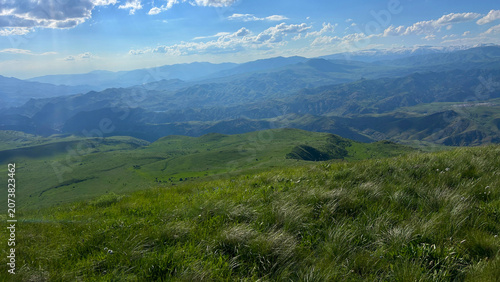 Panoramic Green Highland Valley with Mountains and Cloudy Sky