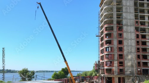 Lifting construction hoist elevator attached to a high-rise residential building under construction near a river on a sunny day