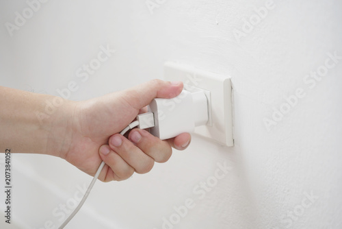 close up hand plugging adapter charge the battery with outlet socket plug and hold mobile phone on wall ,electric safety concept