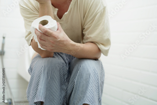 portrait of a man suffers from diarrhea his stomach painful. ache and problem. hand hold tissue paper roll in front of toilet bowl. constipation in bathroom. Hygiene, health care concept.	
