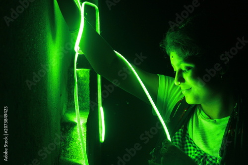 Creative portrait of a young Indian girl illuminated by vibrant green neon LED lights against a dark background. The dramatic lighting creates a futuristic atmosphere