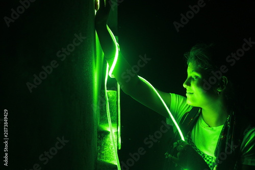 Creative portrait of a young Indian girl illuminated by vibrant green neon LED lights against a dark background. The dramatic lighting creates a futuristic atmosphere