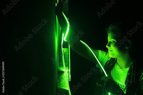 Creative portrait of a young Indian girl illuminated by vibrant green neon LED lights against a dark background. The dramatic lighting creates a futuristic atmosphere