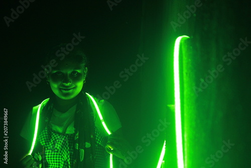 Creative portrait of a young Indian girl illuminated by vibrant green neon LED lights against a dark background. The dramatic lighting creates a futuristic atmosphere