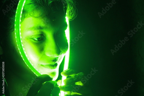Creative portrait of young Indian woman framed by glowing green LED light against black background. Dramatic neon illumination creates futuristic and artistic atmosphere