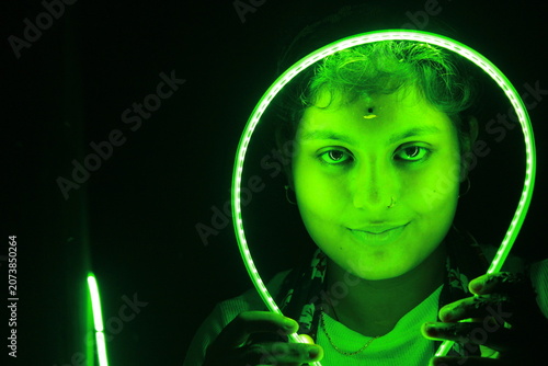 Creative portrait of young Indian woman framed by glowing green LED light against black background. Dramatic neon illumination creates futuristic and artistic atmosphere