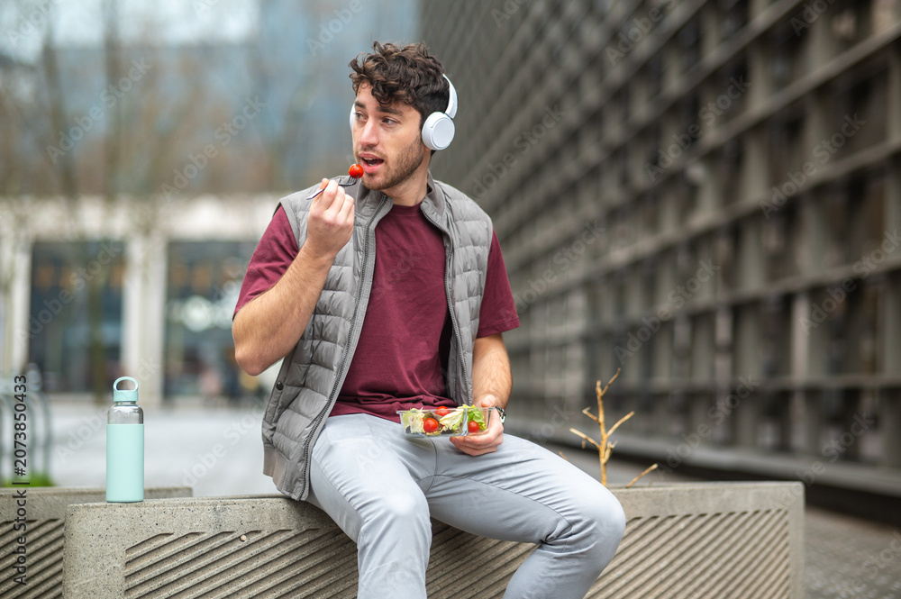 Fototapeta premium Young man eating healthy salad for urban lunch break