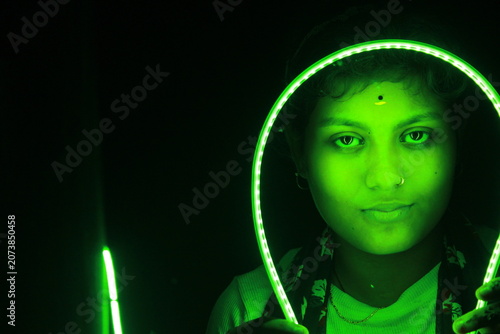 Creative portrait of young Indian woman framed by glowing green LED light against black background. Dramatic neon illumination creates futuristic and artistic atmosphere