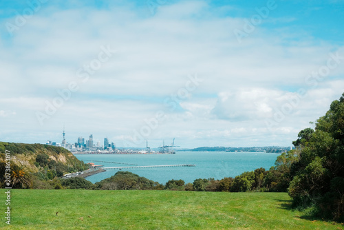 Auckland, New Zealand: panoramic travel view from green grass lawn at Bastion Point toward Waitemata Harbour ocean and distant city CBD skyline.