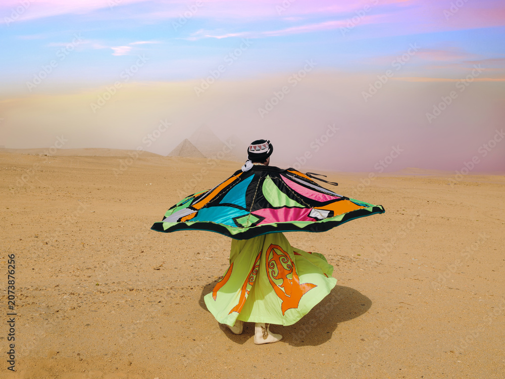 Fototapeta premium Whirling dervish dancer mid spin twirling a colorful tanoura skirt in the Egyptian desert before the Giza pyramids under a pastel sky ideal for