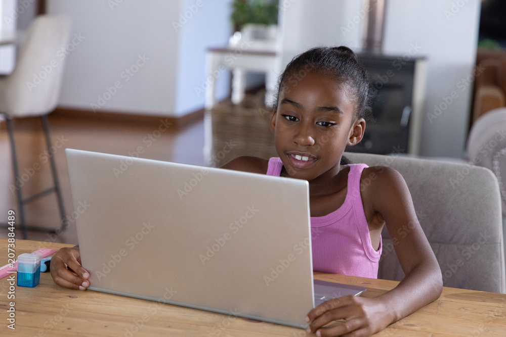 Obraz premium Preteen African American girl sitting at home table using silver laptop, wearing pink top, ruler