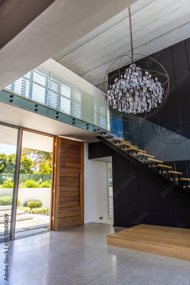 Obraz premium Floating staircase cantilevering from dark wall with glass rail, pivot door opening to yard
