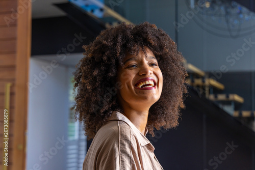 Konstfotografi African American woman smiling and looking up while standing inside modern foyer