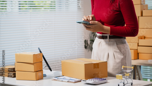 Foto Woman in a home office packing parcel boxes and using a smartphone at a work table, showing small business shipping, online orders, and e-commerce fulfillment